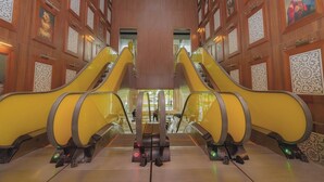 A hotel lobby with two central escalators, wooden paneling, and decorative wall panels. - Luxurious 1BR w/ Balcony and Ocean View – Yoo Panama (Panamá)