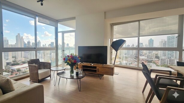 A spacious living room with large windows, a flat-screen TV, a dining area, and a city view.