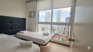 A hotel room with two beds, a large window with a city view, and a modern headboard.