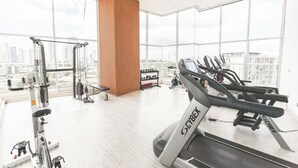 A modern gym with cardio equipment, weight machines, and a large window offering a city view.