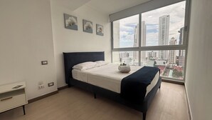 A modern bedroom with a large window, a bed with white linens, a dark headboard, and a small bedside table. - Stunning 3BR with Views, Balcony and Parking (Panamá)