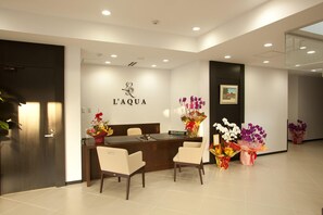 A reception area with a desk, two chairs, and a wall-mounted sign reading "L'AQUA". - Hotel De L Aqua (Miyakojima)