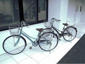 Two bicycles parked on a tiled floor next to a building with large windows and a door. - Hotel De L Aqua (Miyakojima)