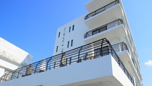 Un hotel moderno con fachada blanca, varios balcones y entrada de piedra.