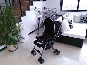 A modern living room with a black stroller, a white sofa with patterned cushions, a potted plant, and a staircase in the background. - Hotel De L Aqua (Miyakojima)