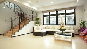 Una sala de estar moderna con una escalera, un conjunto de sofá, una mesa de centro y ventanas amplias.