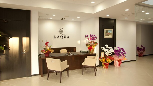 Un área de recepción con un mostrador, dos sillas y un cartel en la pared que dice "L'AQUA".