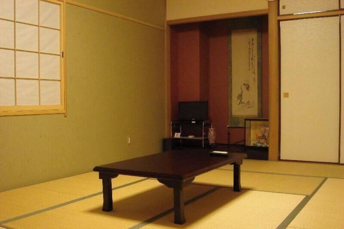 Una habitación japonesa tradicional con suelo de tatami, una mesa baja, un televisor y una puerta corredera.