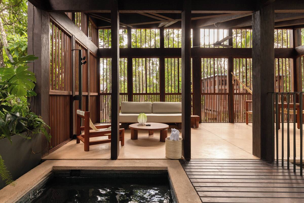 Una terraza de madera con zona de estar, una piscina pequeña y vistas de la vegetación circundante.