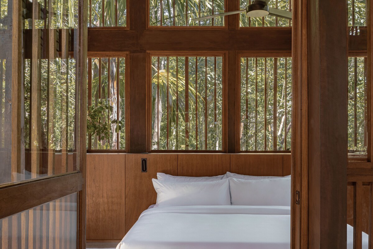 Une chambre avec un lit, des boiseries et de grandes fenêtres donnant sur un paysage verdoyant.