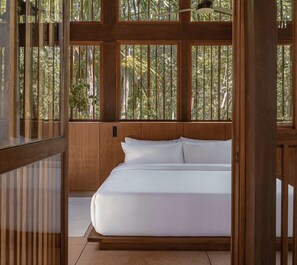 Une chambre avec un lit, des boiseries et de grandes fenêtres donnant sur un paysage verdoyant.