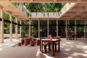 Un área de patio techada al aire libre con macetas de terracota, mesas y bancos de madera.