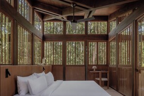 Una habitación de madera con una cama, un ventilador de techo y ventanas amplias.