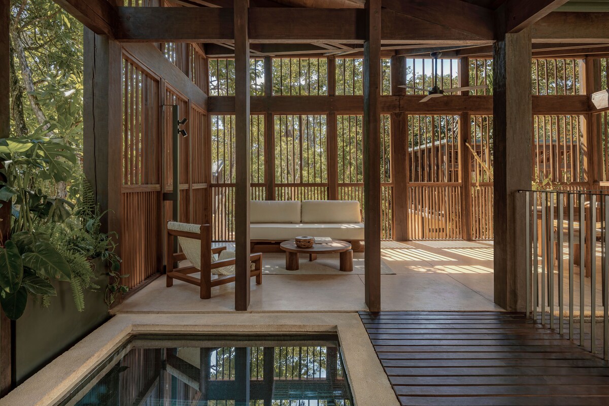 Una terraza de madera con un sofá, sillas, una mesita y una piscina.