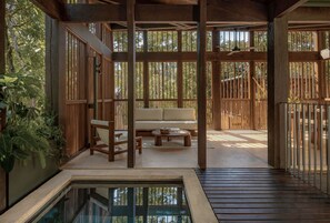 Una terraza de madera con un sofá, sillas, una mesita y una piscina.