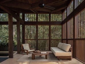 Un espacio exterior techado con techo de madera, un sofá, una silla y una mesa.