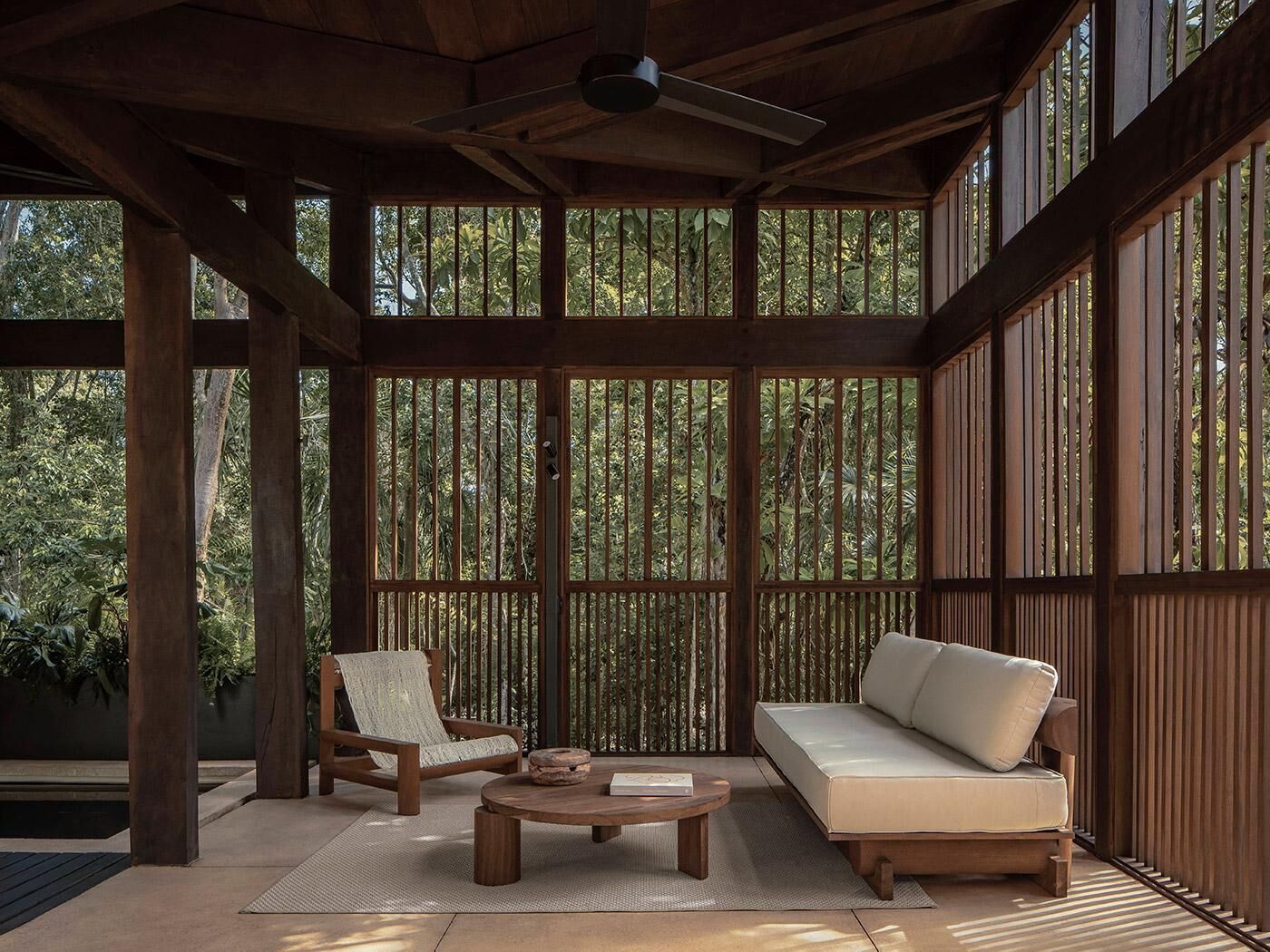 A covered outdoor seating area with a wooden ceiling, a sofa, a chair, and a table.