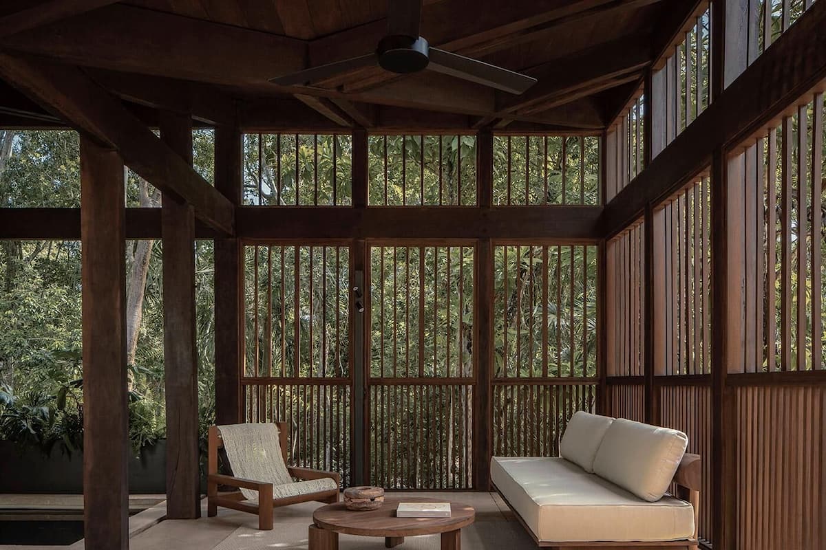 Un espacio exterior techado con techo de madera, un sofá, una silla y una mesa.