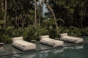 Un espace aménagé au bord de la piscine, comprenant trois chaises longues et une petite table, le tout entouré d’une végétation tropicale luxuriante.