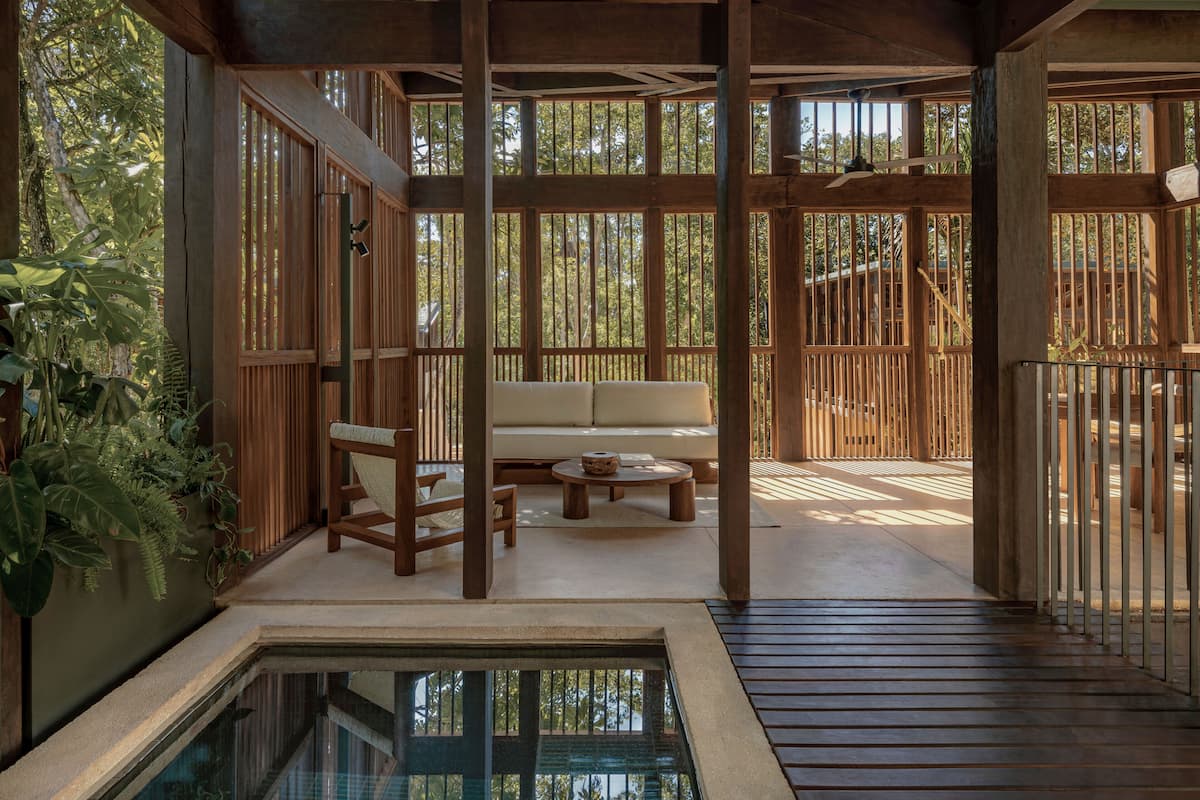 Una terraza de madera con un sofá, sillas, una mesita y una piscina.