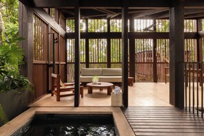 Una terraza de madera con zona de estar, una piscina pequeña y vistas de la vegetación circundante.