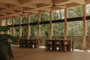 Un espace extérieur aménagé, abrité et doté de mobilier en bois, offrant une vue sur un feuillage dense à travers de grandes fenêtres.