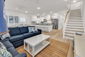 A modern living room with a sofa, coffee table, and a staircase leading to an upper level. - My Happy Place - 2nd Row NEW construction in Garden City Beach (Garden City Beach)