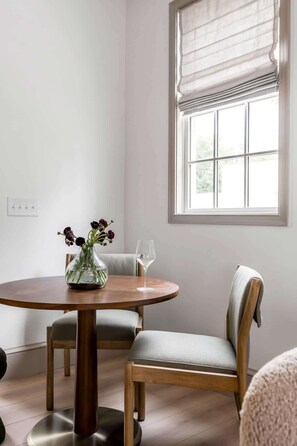 A dining area with a round wooden table, two upholstered chairs, a vase with flowers, and a wine glass. - Spacious 4bd House, New Bathrooms, Near King St. (Charleston)