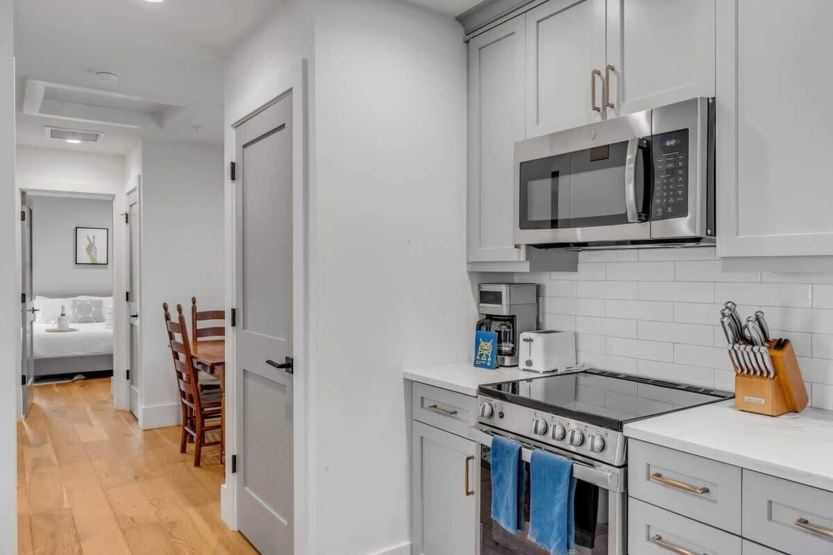 A modern kitchen with white cabinets, a stainless steel microwave, a gas stove, and a coffee maker.