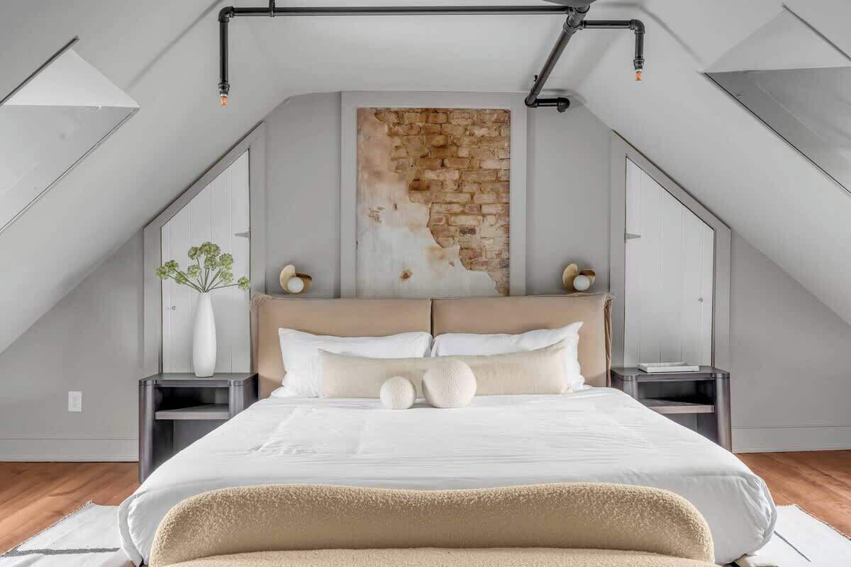 A modern bedroom with a sloped ceiling, a large bed, a stone accent wall, and a skylight.