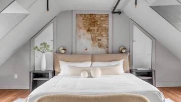 A modern bedroom with a sloped ceiling, a large bed, a stone accent wall, and a skylight.