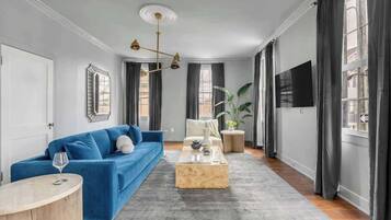 A modern living room with a blue sofa, a wooden coffee table, and a large window with curtains.
