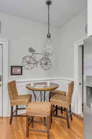 Un coin repas avec une table ronde, quatre chaises en osier, un luminaire suspendu et une décoration murale représentant un vélo.