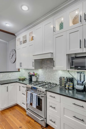 A modern kitchen with white cabinets, a stainless steel stove, a microwave, and a coffee maker. - Downtown Suite in Pristine Historic Home (Charleston)