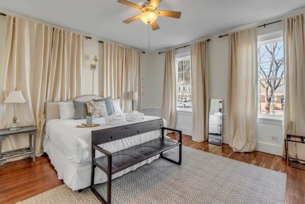 Une chambre à coucher avec un lit, des tables de chevet, un ventilateur de plafond et une vue sur l’extérieur.