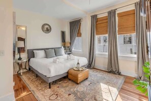 Une chambre à coucher avec un lit, des tables de chevet, un miroir et une fenêtre avec des rideaux.