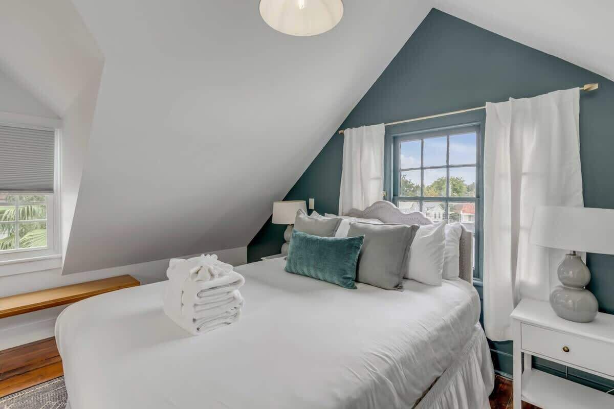 A bedroom with a bed, pillows, a nightstand, a lamp, and a window with curtains.