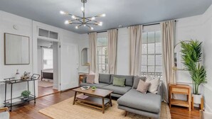 Una sala de estar moderna con un sofá gris, una mesa de centro de madera, una lámpara colgante y un ventanal con cortinas.