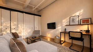 Ein modernes Wohnzimmer mit einer Couch, einem Couchtisch, einem an der Wand befestigten Fernseher und einem kleinen Beistelltisch mit einer Lampe.