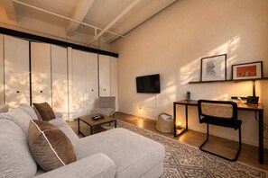 Een moderne woonkamer met een bank, een salontafel, een aan de muur bevestigde televisie en een bijzettafeltje met een lamp.