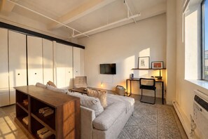 Ein modernes Wohnzimmer mit Sofa, Couchtisch, Bücherregal, Fernseher und einem kleinen Tisch mit Lampe.