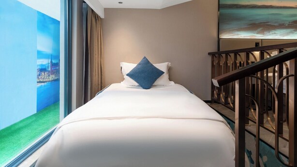 A hotel room with a bed, a view of a cityscape through a large window, a painting on the wall, and a staircase with a railing. - Echerm Hotel Wuyangcun Metro Station (Guangzhou)