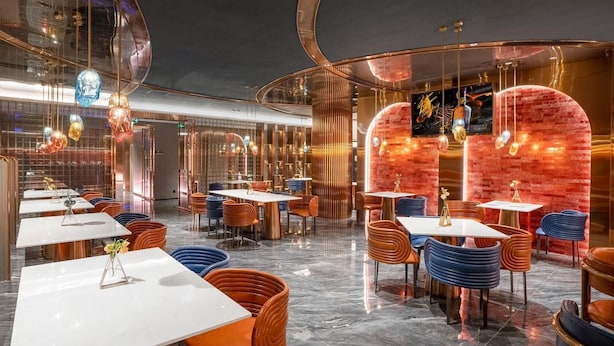 Un interior de restaurante moderno con suelos de mármol, varias mesas de comedor y sillas de colores.