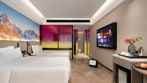 Habitación de hotel con dos camas, televisión, escritorio y un florero, además de un mural de colores en la pared.
