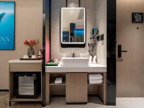 Un baño moderno con un espejo grande, un lavamanos, un perchero para toallas y un mueble pequeño.