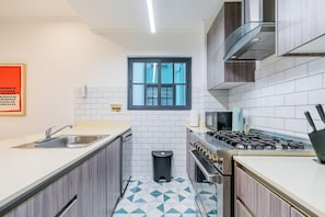 Une cuisine compacte avec des carreaux blancs, une fenêtre, un évier, une cuisinière et une poubelle.
