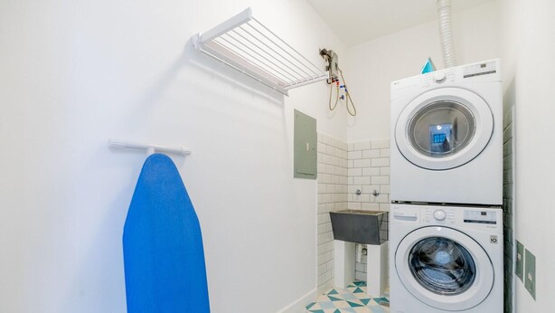 A laundry room with two stacked washing machines, a drying rack, and a tiled floor. - Casa Quijano 06 By Wynwood House (Panama City)