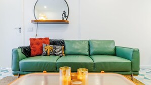 A green leather sofa with patterned cushions, a round mirror above it, and a table with candles. - Casa Quijano 06 By Wynwood House (Panama City)