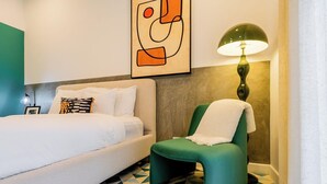 A hotel room with a bed, a green armchair, a geometric patterned floor, a wall art piece, and a lamp. - Casa Quijano 06 By Wynwood House (Panama City)