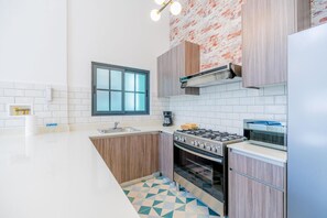 A modern kitchen with white countertops, a gas stove, an oven, and a microwave. There is a window above the sink and a light fixture above the stove. - Casa Quijano 06 By Wynwood House (Panama City)